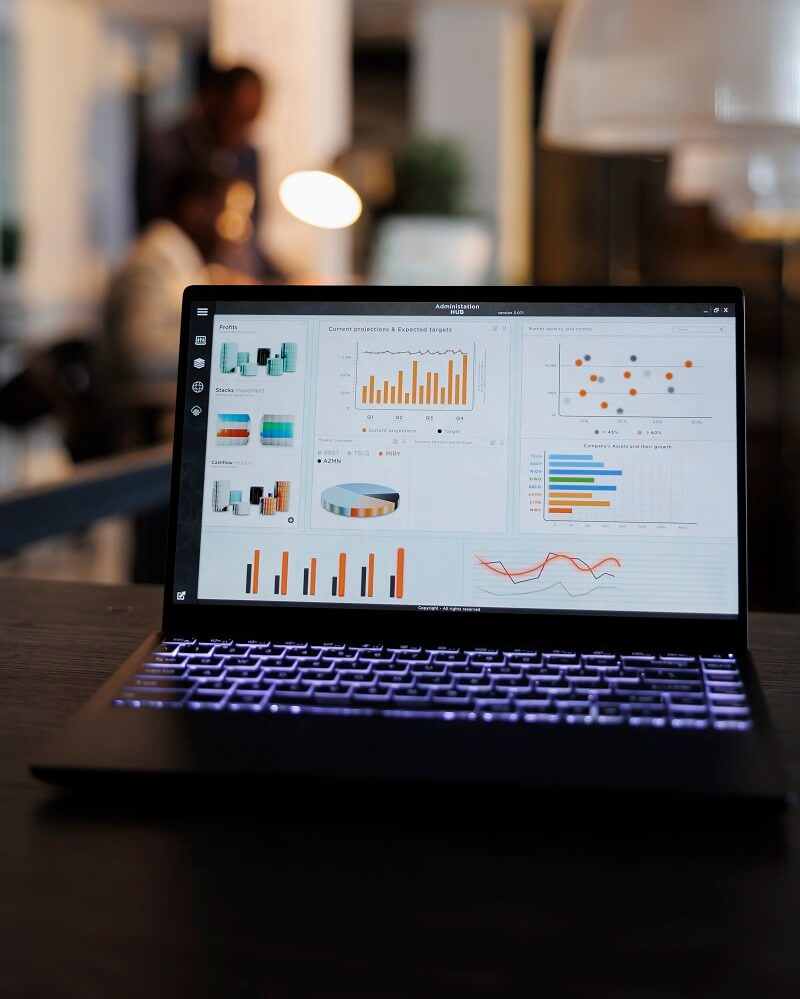 laptop-computer-with-marketing-statistics-graphs-screen-standing-table-startup-office-coworkers-discussing-company-strategy-background-employees-working-overtime-startup-office (1)
